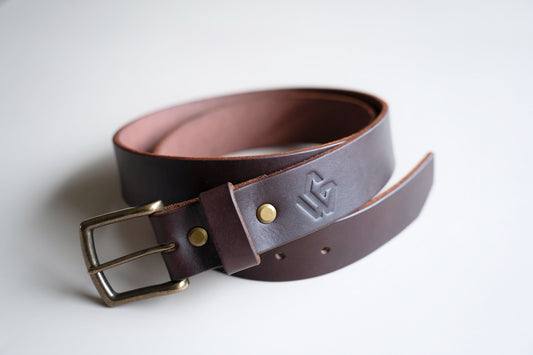Four Timeless Belts in black, medium brown, and dark brown colors lying flat on a grey background, showcasing their durability and classic design. | Quatre Timeless Belts en noir, brun moyen et brun foncé posées à plat sur un fond gris, mettant en valeur leur durabilité et leur design classique.